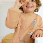 Kind trägt einen honiggelben Pullover mit Tiermotiv von People Wear Organic